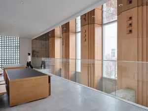A bright and open interior space with a large glass wall, wooden elements, and natural light, featuring two people and seating areas