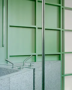 A modern bathroom with a sink, mirror, and shower area, featuring a green painted wall and modern design