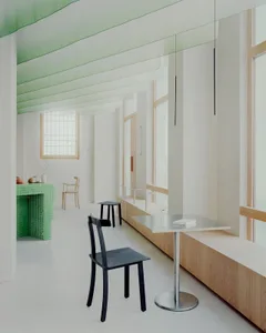 Empty white room with green accents, two chairs, a dining table, and a potted plant, exuding a clean and minimalistic atmosphere