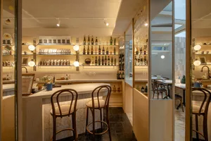 A warm and inviting bar area with wooden walls and flooring, featuring a bar counter with bottles and two chairs