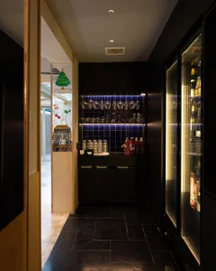 Dark kitchen with a refrigerator, bottles, cups, and an open doorway to another room