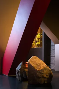 A large rock on a platform in front of a bold red wall, creating a modern and minimalist interior design space