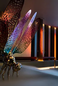 A metal sculpture of a dragon with a butterfly design sits on a table near a wall, surrounded by a chair and two benches in a contemporary setting