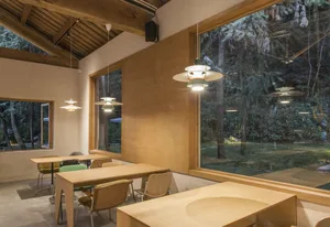 A warm and inviting restaurant interior with wooden tables and chairs, large windows, and natural light