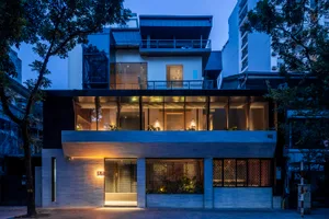 A modern building with multiple levels, a rooftop terrace, and a mix of concrete, glass, and wood materials, featuring ample natural light through numerous windows