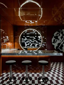 A modern bar with a circular countertop, a large mirror above, and three stools, featuring a combination of wood and metal elements, with warm lighting creating a cozy atmosphere