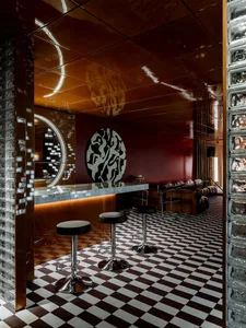 Modern bar area with a checkered pattern on the walls, two stools in front of a countertop, and three chairs arranged around the space