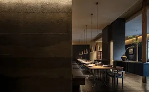 A modern restaurant with a large dining table surrounded by chairs, lit by hanging lights