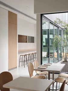 A modern kitchen and dining area with white walls, wooden floors, and a dining table surrounded by chairs, with a kitchen section featuring a sink and countertops