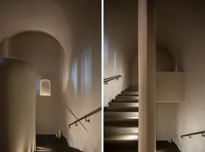 A stone wall with a black and white photo of a staircase on one side and a rendered architectural scene of the same staircase on the other, featuring a metal railing