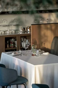 Elegant dining area with a white tablecloth, wine glasses, and dinnerware, surrounded by bottles and two chairs