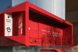A modern red building with a metal staircase leading to a doorway, surrounded by a neutral background