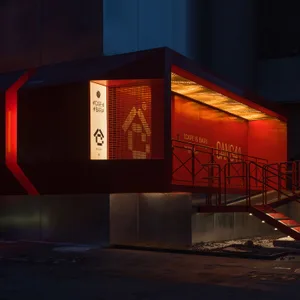 A modern building with a red exterior, featuring a large window and two sets of stairs, set in a contemporary urban environment
