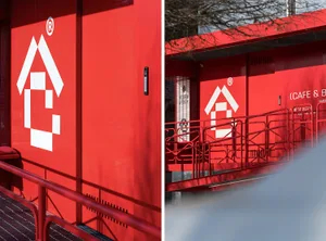 A modern building with a red wall and white door, made of concrete, with clean lines and minimalistic design elements, well-lit and welcoming
