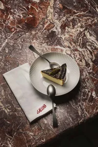 A marble tabletop with a slice of cake on a white plate, two spoons, and an elegant indoor dining setting