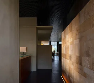Dimly lit modern hallway with a stone wall, glass door, and two chairs creating a cozy seating area