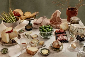 一張擺滿各式美食的餐桌，包括起司、肉類、蔬菜和其他菜餚，桌上還放了幾瓶飲料
