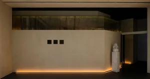 Interior design featuring a concrete wall with three square windows, two vases, and a bench in a modern industrial space