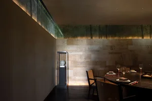 A well-lit and inviting restaurant dining area with a long wooden table and chairs, surrounded by wine glasses, ready to host guests