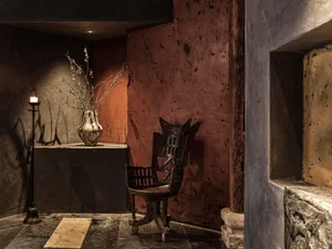 A cozy living space with a wooden chair and a vase on a table, set against a wall