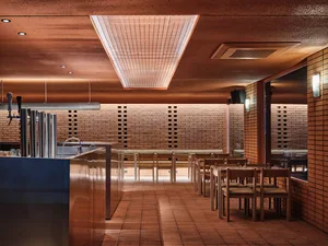 Modern restaurant interior with wooden floors and walls, featuring multiple dining tables and chairs in a warm and inviting atmosphere