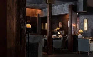 A dimly lit dining area with a large wooden table and multiple chairs, set up for a meal, creating a cozy and inviting atmosphere