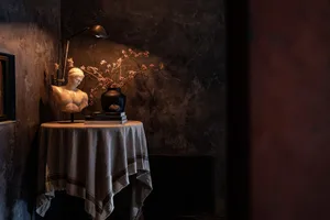 A small table with a vase of flowers and books in a cozy living area or study with a statue and decorative atmosphere