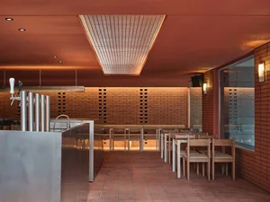 Warm and inviting restaurant interior with brick walls, red ceiling, dining tables, chairs, and a kitchen area with a refrigerator and oven
