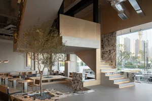 Modern interior space with concrete walls and flooring, featuring a staircase, chairs, and a dining table in a spacious and minimalistic atmosphere