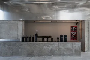 Industrial kitchen with concrete floor, multiple speakers, coffee makers, and decorative vase, giving a modern and industrial feel