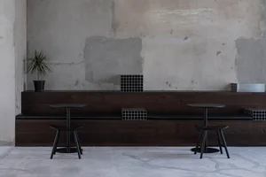 A restaurant interior with a wooden dining table, black chairs, and brick-patterned walls, creating a stylish and comfortable atmosphere for dining and socializing