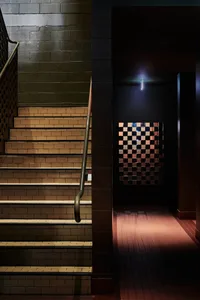A hotel staircase with two sets of wooden stairs leading to a darker hallway, surrounded by a cozy and inviting atmosphere