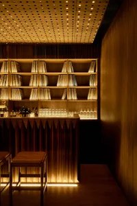 A cozy bar area with a wooden countertop, records on display, and wine glasses, set with two chairs for seating