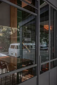 燈光明亮的餐廳內部，配有木質桌椅、金屬裝飾，以及桌上各式物品，背景為玻璃門與自然光線