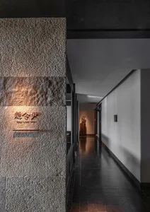 A dimly lit hallway with a stone wall and a wooden door, featuring two statues and a mysterious atmosphere