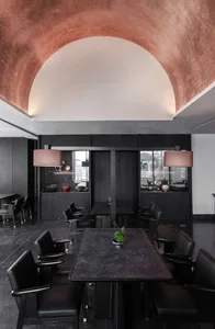 A modern restaurant dining area with a large black table surrounded by multiple chairs and a potted plant, creating a comfortable and inviting atmosphere