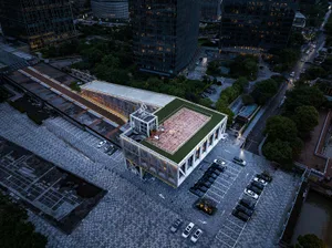 A modern building with a white exterior and a green roof, set against an urban backdrop with parked cars and a contemporary atmosphere