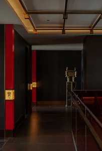 A traditional Asian-style hallway with red walls, black trim, a staircase, and a doorway, featuring two statues and a welcoming atmosphere