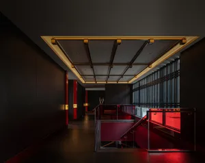 A modern interior space with a glass staircase, black walls, and red accents, featuring a bench at the base of the stairs