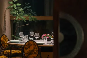 Dining area with a round table set for dinner, surrounded by chairs and decorated with flowers and wine glasses