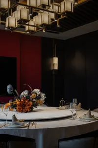 A sophisticated dining area with a round table set with wine glasses, cups, bowls, vases, and potted plants, surrounded by multiple chairs and a refined atmosphere