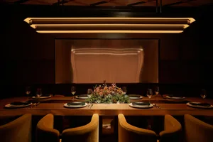 Dining area with a long wooden table, floral centerpiece, and wine glasses, set in a sophisticated restaurant environment