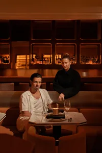 An intimate dining area with a wooden table and chairs, wine glasses, and multiple bottles, set in a relaxed atmosphere