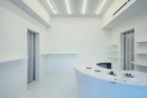 A minimalist kitchen dining space with white surfaces, a large counter, and a sink and refrigerator, giving off a clean and bright atmosphere