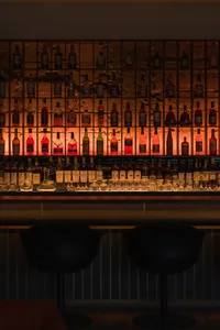 A social bar scene with a long wooden counter, lined with bottles, and comfortable seating for patrons