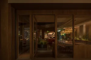 Open living area with wooden floors and walls, featuring a dining table, chairs, and a potted plant, creating a warm and inviting atmosphere