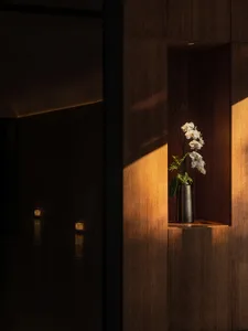 A wooden display case with a vase and flowers in front of a doorway, creating a welcoming atmosphere
