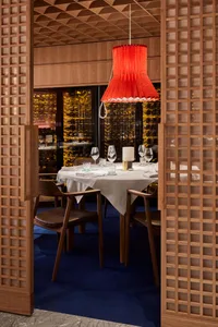 A sophisticated dining area with a wooden table, chairs, wine glasses, cups, and bowls, set in a restaurant environment