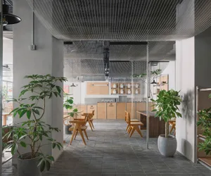 Cozy cafe interior with wooden floors, tables, chairs, and potted plants, featuring a tiled pattern on the walls and well-lit atmosphere