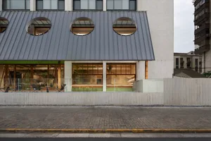 一座現代建築，屋頂有大型懸挑，融合混凝土與玻璃元素，場景中擺放多把椅子供休憩或放鬆
